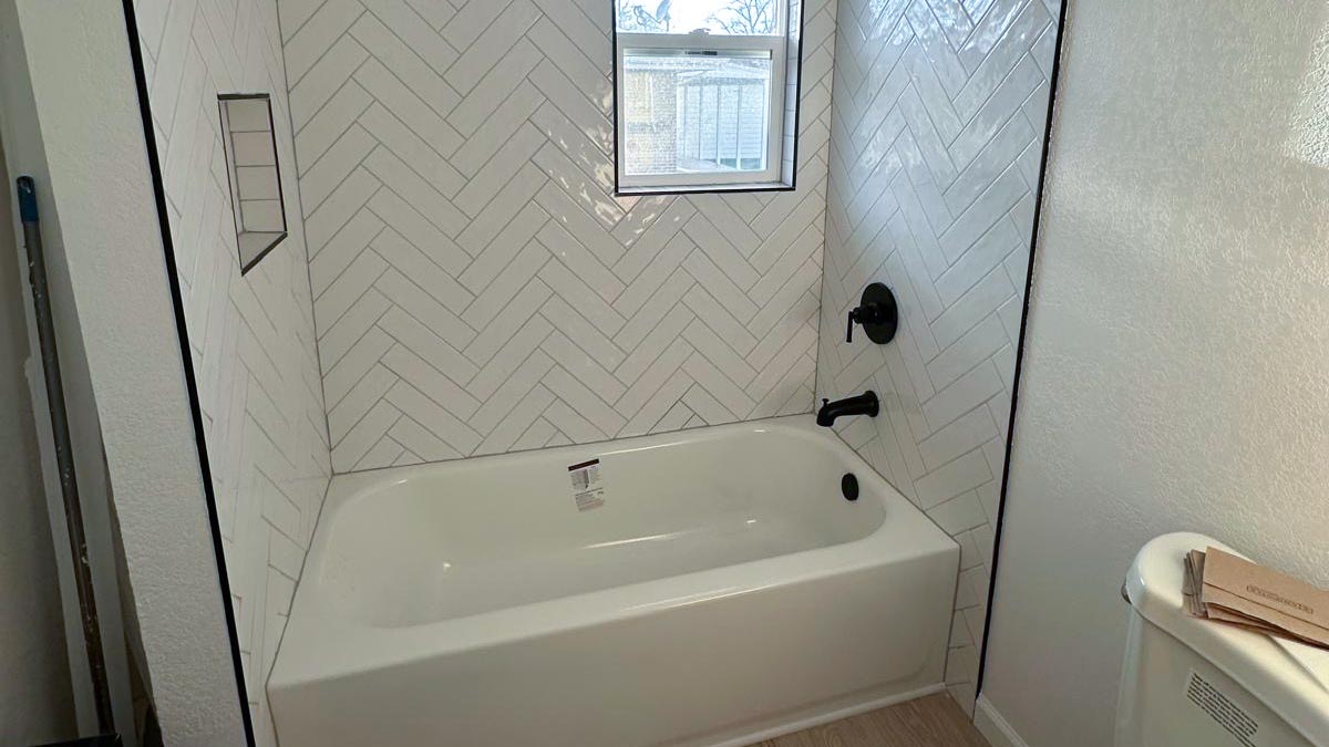 Herringbone Tub Surround Bathtub and shower surround tiled in white herringbone with matte black fixtures and a glass shelf niche
