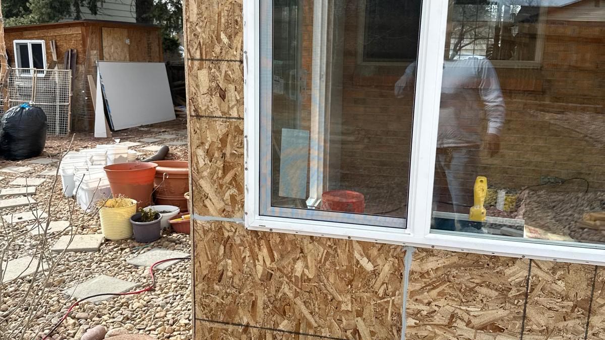 Corner Window Framing Exterior corner of a home mid-remodel showing new window openings in OSB sheathing above a brick base