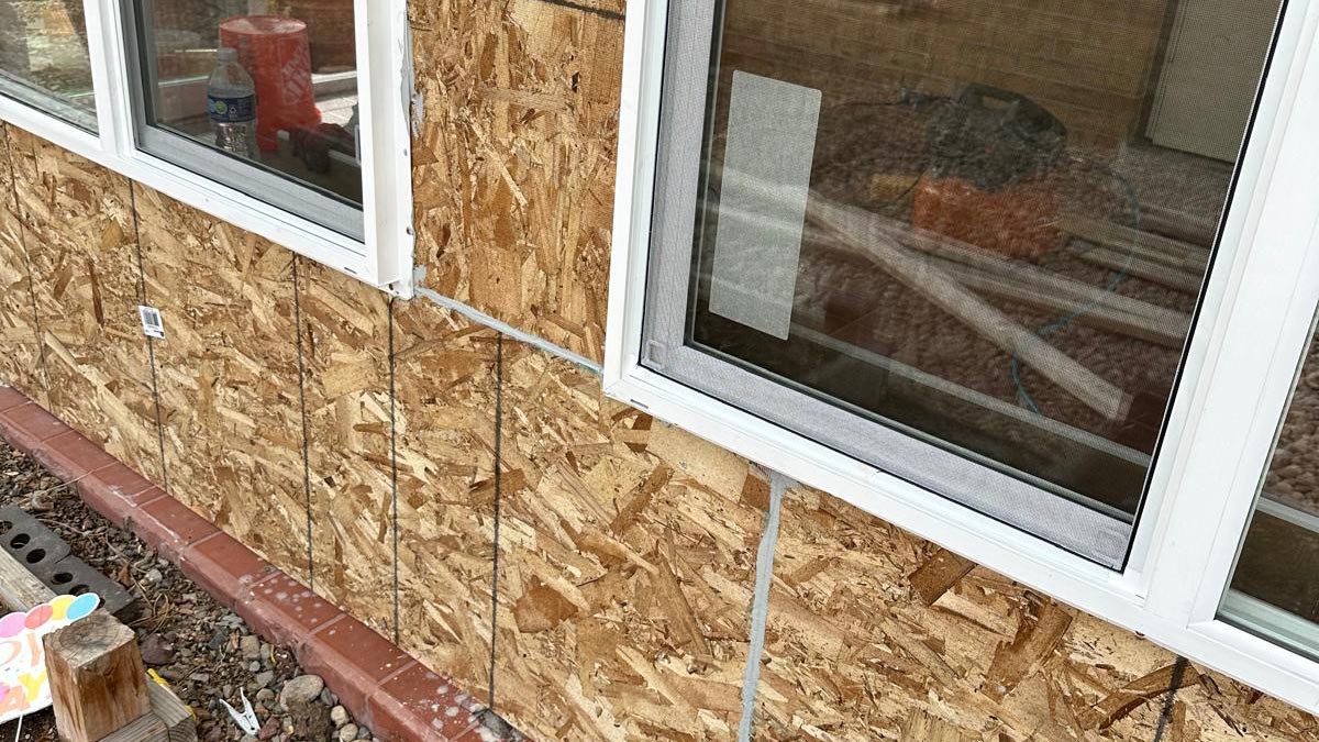 Exterior Re-Side in Progress Home exterior mid-repair with siding removed, OSB sheathing exposed around vinyl windows and brick trim